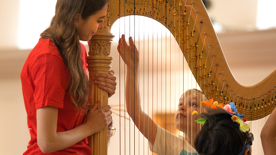 Children at a Sparks event and an RCM student stood looking and holding a harp